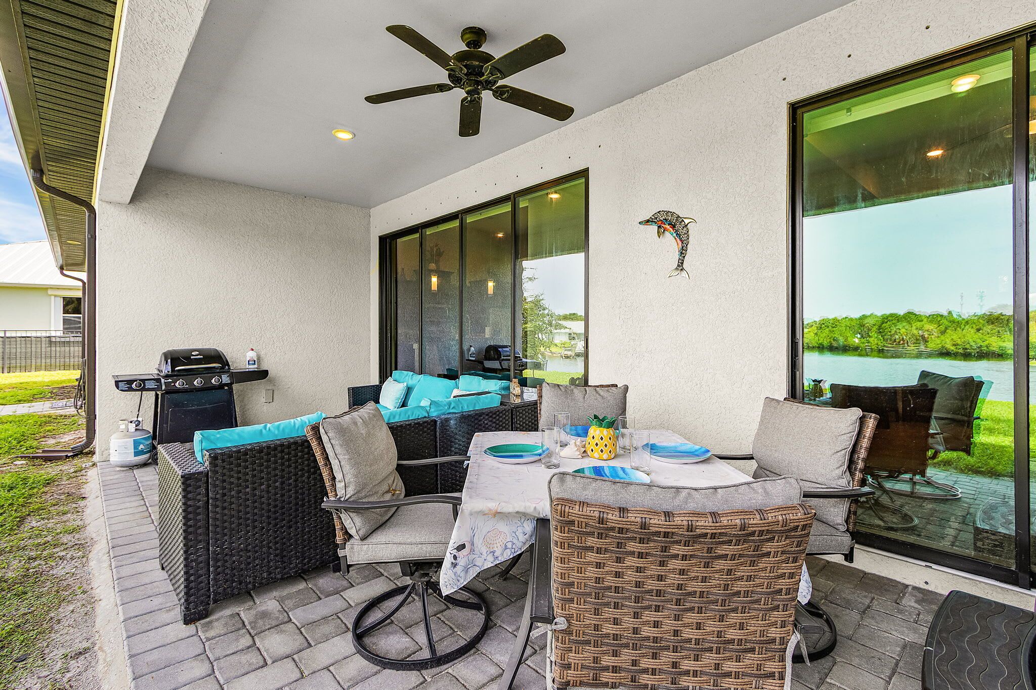 Un patio al aire libre con mobiliario de mimbre, una parrilla y vista a un cuerpo de agua.