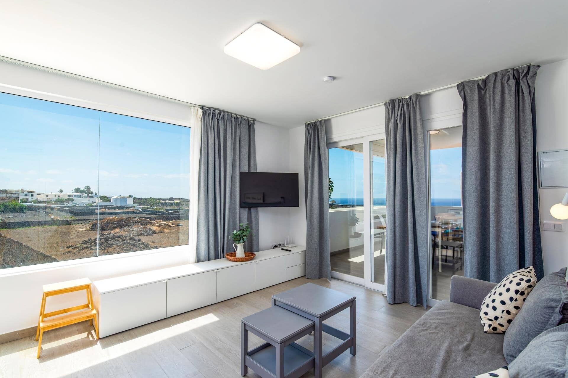 A modern living room with a large window, a flat-screen TV, a sofa, a coffee table, and a small wooden bench.