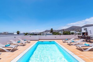 Une piscine sur le toit, dotée de chaises longues et offrant une vue sur la ville et les montagnes.
