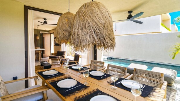 A dining area with a pool view, including a table set for six, wicker chairs, and hanging light fixtures. - Villa Terra Mare Zephyr by Villa Plus (Ialysos)
