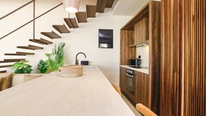A modern kitchen with a wooden staircase, a central island, and a hanging light fixture. - Villa Terra Mare Zephyr by Villa Plus (Ialysos)