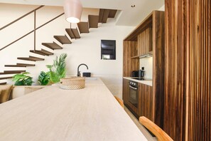 A modern kitchen with a wooden staircase, a central island, and a hanging light fixture. - Villa Terra Mare Zephyr by Villa Plus (Ialysos)