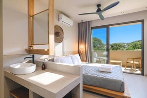 A hotel room with a large window, a bed, a bathroom with a sink and mirror, and a ceiling fan. - Villa Terra Mare Zephyr by Villa Plus (Ialysos)