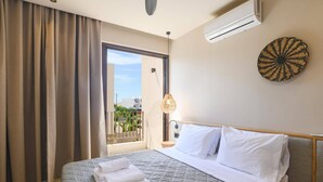 A hotel room with a bed, a window with curtains, an air conditioning unit, a wall-mounted lamp, and a decorative wall piece. - Villa Terra Mare Zephyr by Villa Plus (Ialysos)