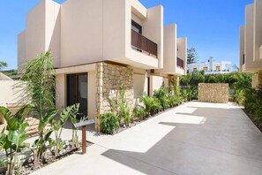 Un edificio moderno con fachada de piedra, sendero de hormigón y abundante vegetación.