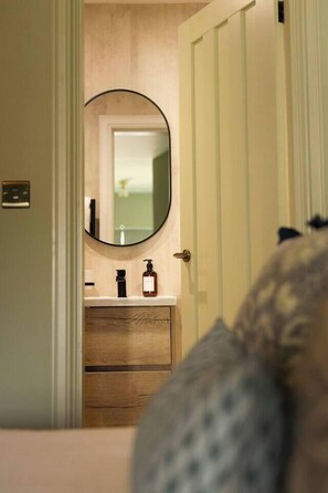 A bathroom with a wooden vanity, a round mirror, and a door leading to another room.
