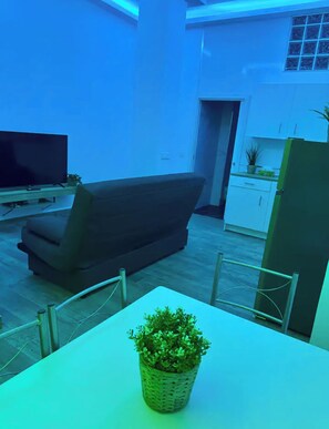 Ein Wohnzimmer mit Sofa, Flachbildfernseher, Esstisch mit Stühlen und einer Zimmerpflanze.
