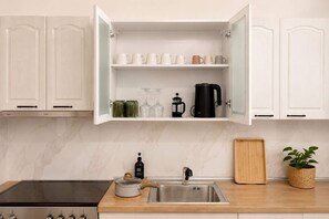 Una cocina con armarios blancos, una cafetera negra y una tabla de cortar de madera.
