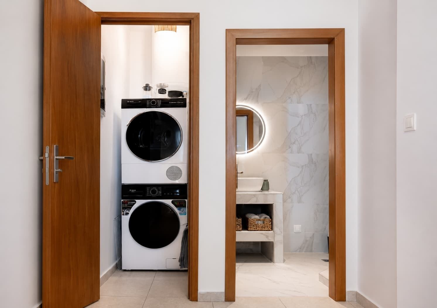 Un lavadero con lavadoras y secadoras apiladas, un espejo sobre el lavabo y un marco de puerta de madera.