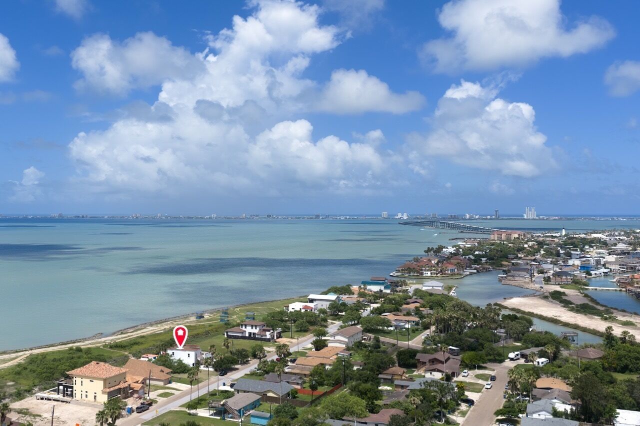 Un pueblo costero con edificios residenciales, un puerto deportivo y un puente a lo lejos.