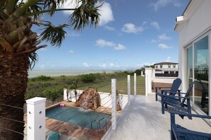 Ein Poolbereich mit Blick aufs Meer, eine Palme und ein Gebäude mit Balkon.