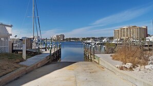 A marina with a concrete walkway leading to a dock, surrounded by buildings and boats. - 🌴Sandpiper Cove 8242~Steps to the beach- 5 Pools + 3 Hot Tubs~ Golf Course ⛳ (Destin)