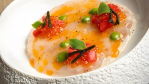 A white bowl with a textured exterior containing a dish with green peas, red tomatoes, and a liquid.