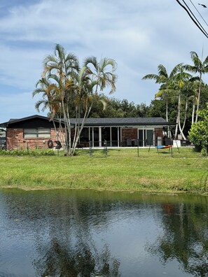 A modern house with a brick exterior, a garage, and a fenced yard with palm trees. - Heated pool, Putting Green, propane fire pit, outdoor shower waterfront home 4 U (Palm Beach Gardens)