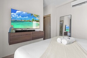 Ein Hotelzimmer mit Bett, Fernseher auf einer Holzkommode, Spiegel und Blick auf einen Strand.