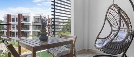 A balcony with a wooden table, chairs, a hanging chair, and a view of modern buildings.