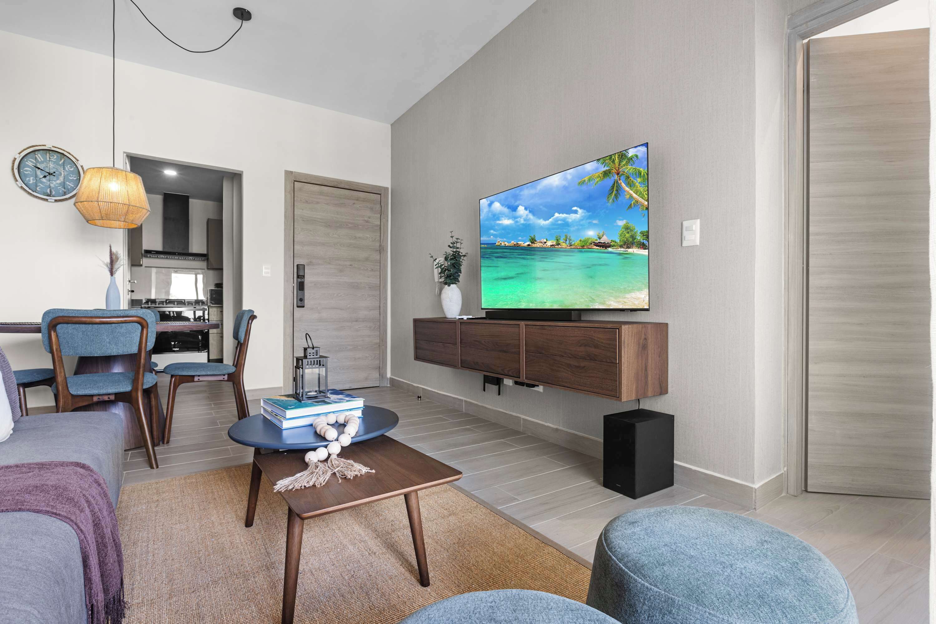 A modern living room with a flat-screen TV, a dining area, and a kitchen in the background.