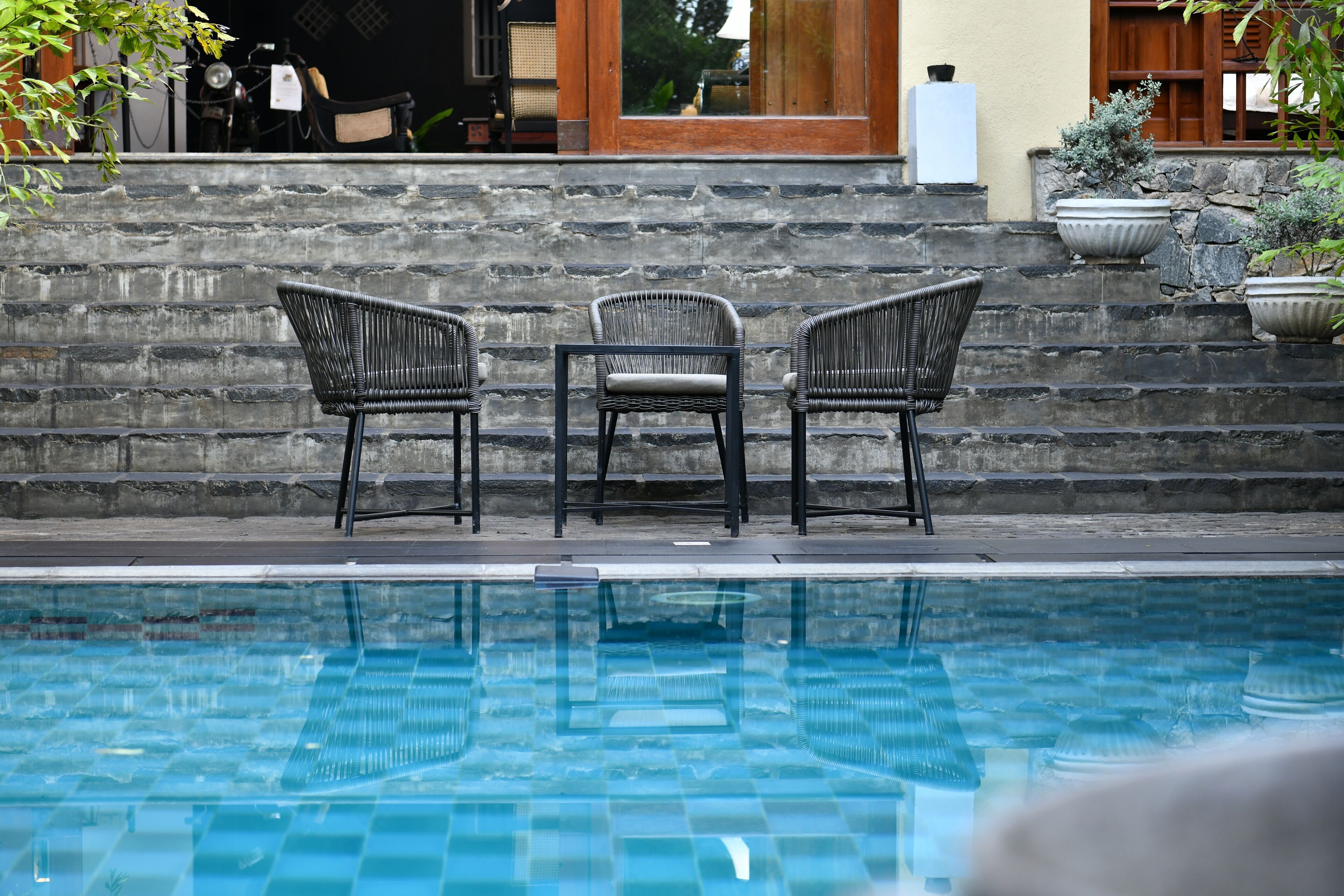 A poolside area with three wicker chairs and a stone wall.