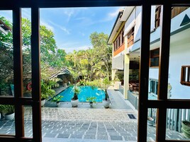 Vista de una piscina rodeada de plantas en macetas y una pérgola, con un edificio al fondo.