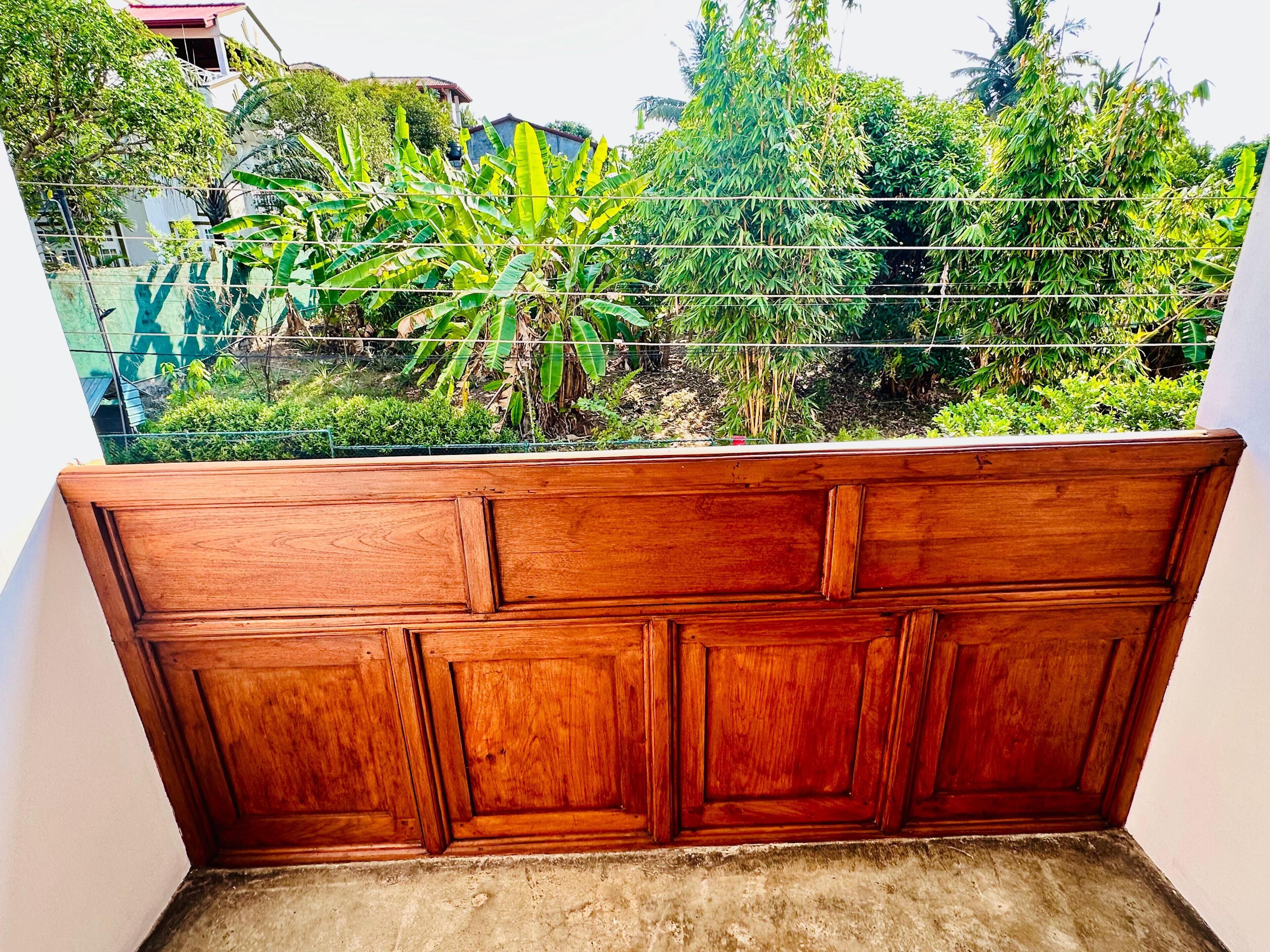 Un banco de madera con vistas a un jardín con diversas plantas y un edificio al fondo.