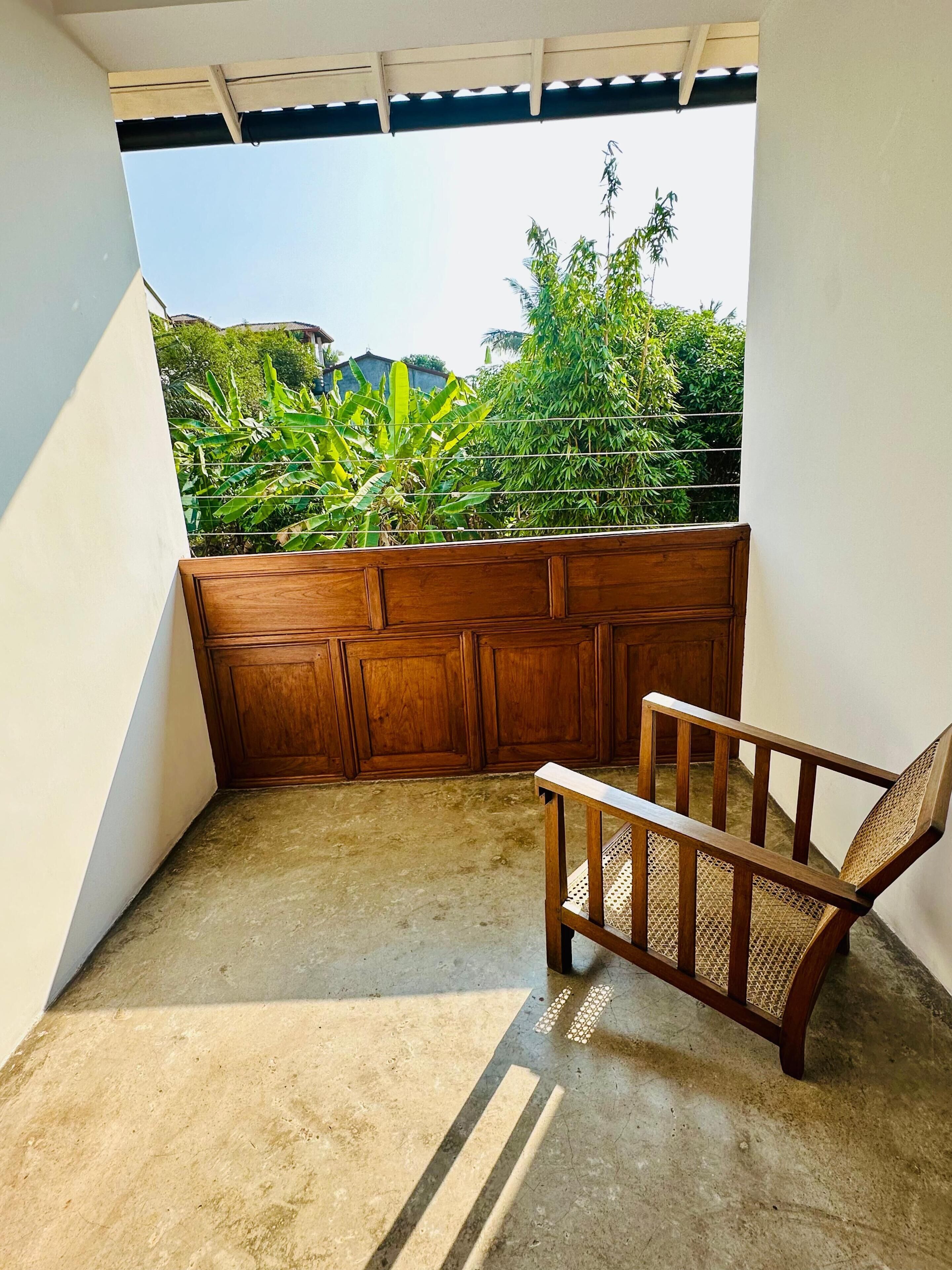 A room with a concrete floor, a wooden bench, a wooden partition, and a view of greenery outside.