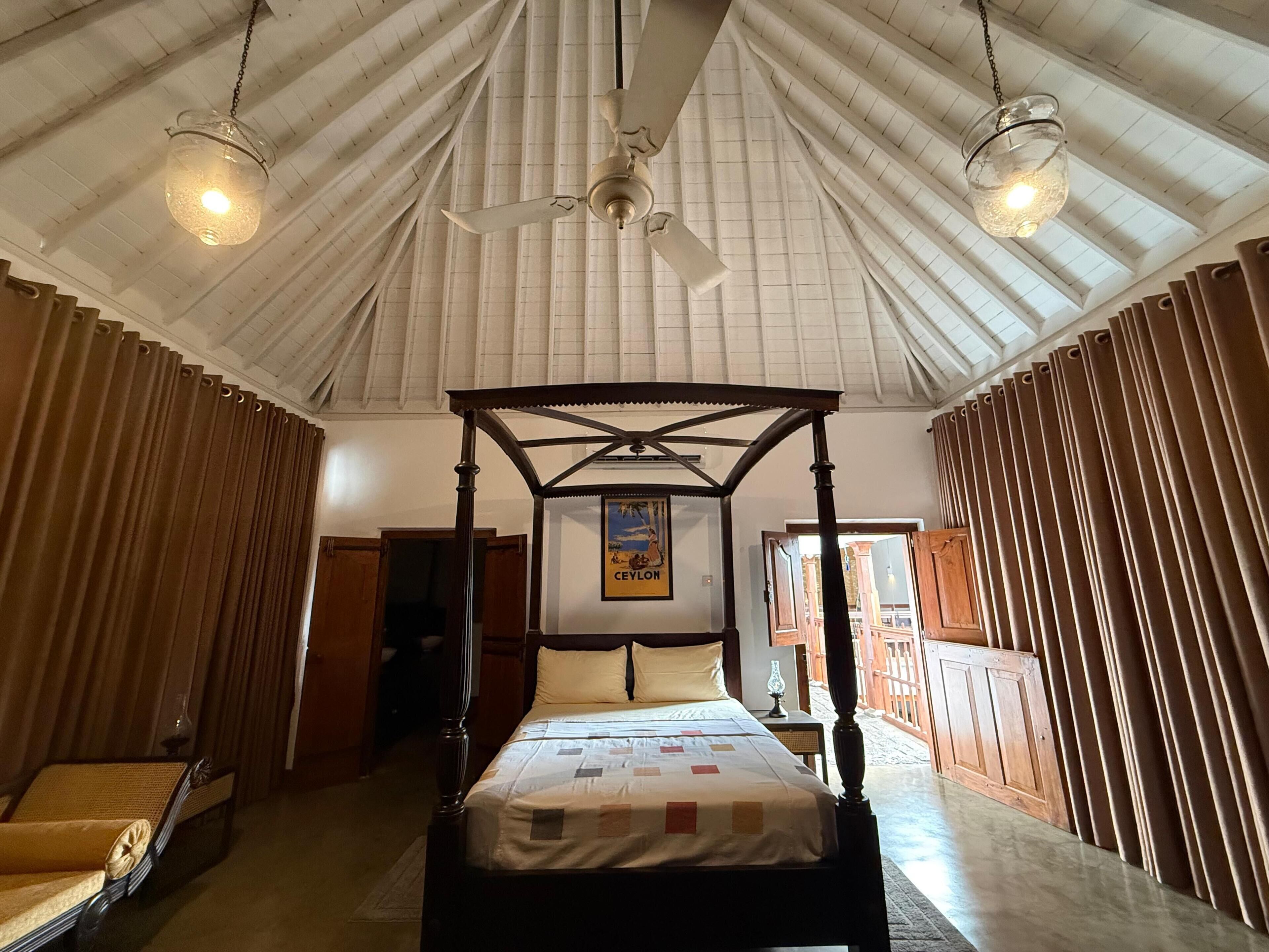 A four-poster bed with a canopy, a ceiling fan, and a poster on the wall.