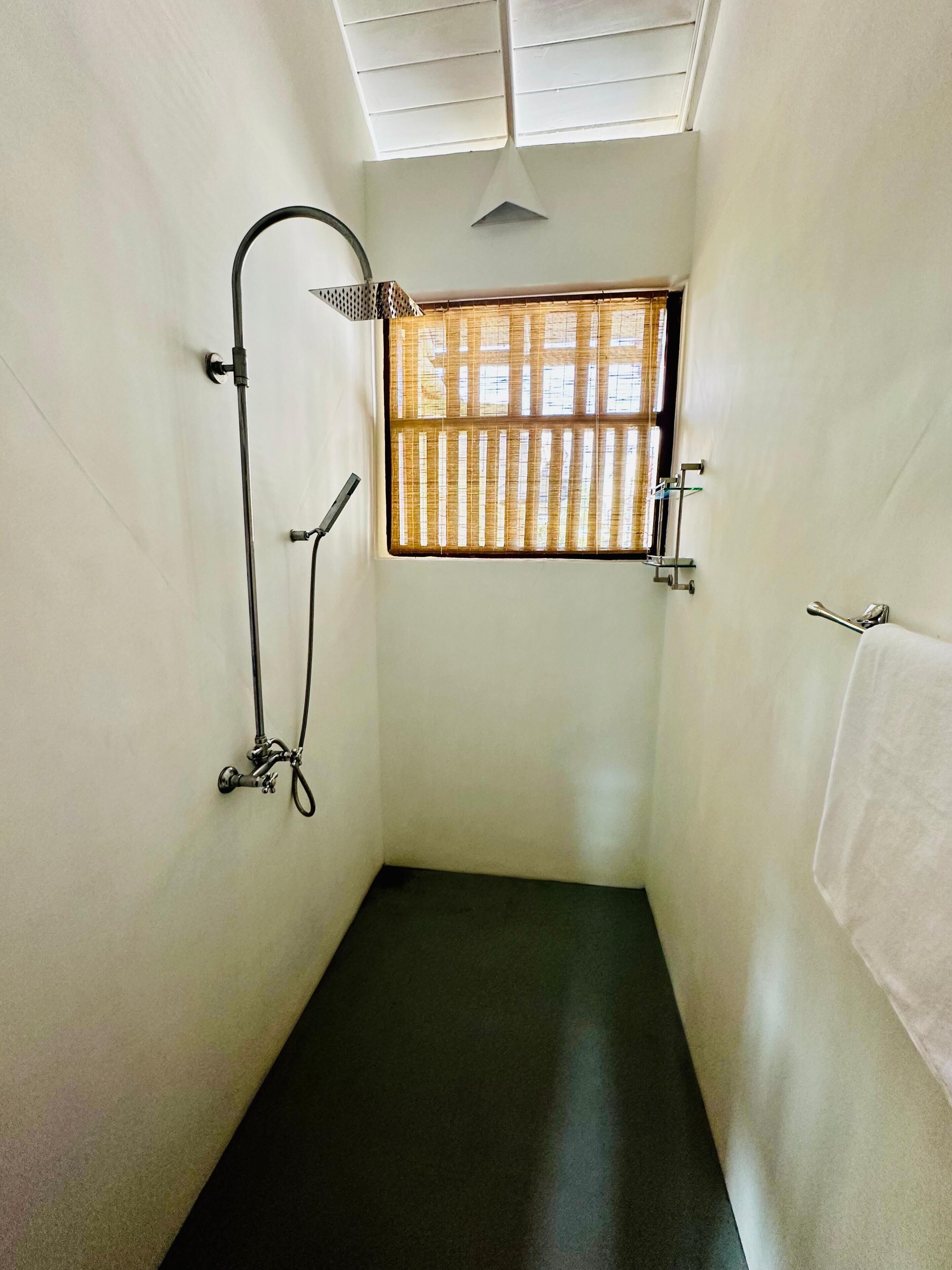 A small, narrow shower room with a window, a towel rack, and a ceiling vent.