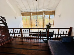 Una habitación con piso de madera, un banco, un sofá, un ventilador y una ventana con persianas de bambú.