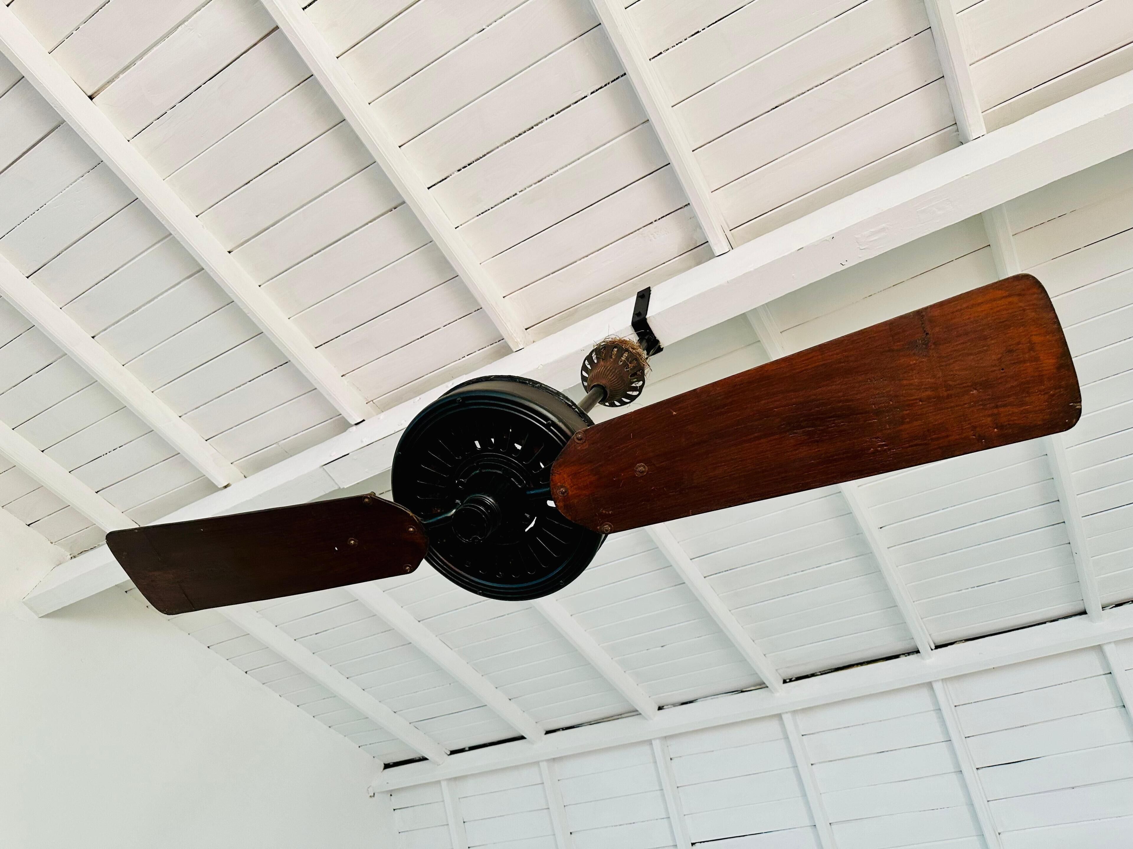 A ceiling fan with wooden blades and a central motor, mounted on a white ceiling with a grid pattern.