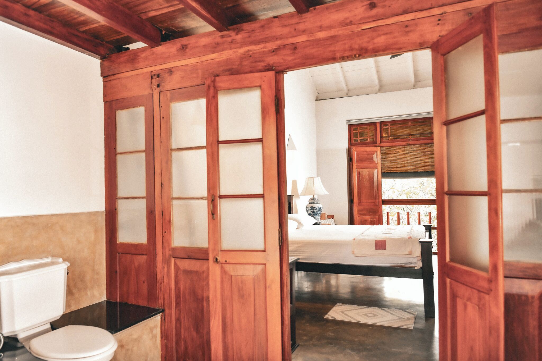 A traditional wooden room with a toilet, a bed, and a window.