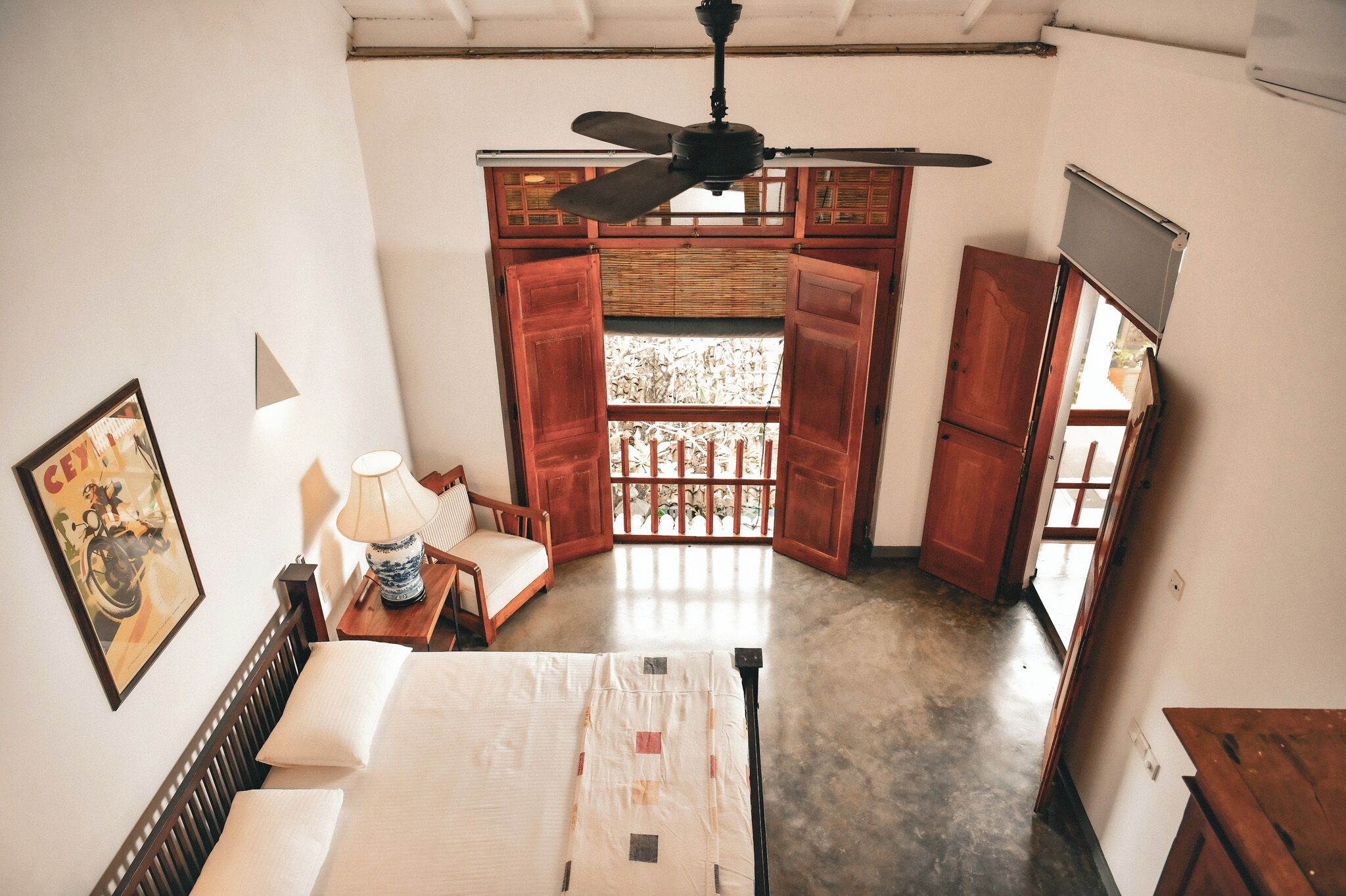 A room with a bed, a ceiling fan, a window with open shutters, and a framed picture on the wall.