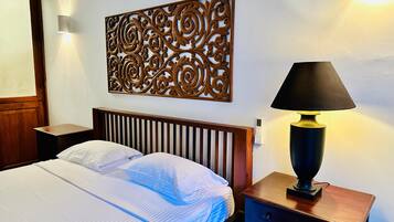 Ein ordentlich bezogenes Bett mit weißen Bettwäsche, ein Holz-Kopfteil, eine Wandverkleidung, ein Nachttisch mit Lampe und ein Thermostat an der Wand.