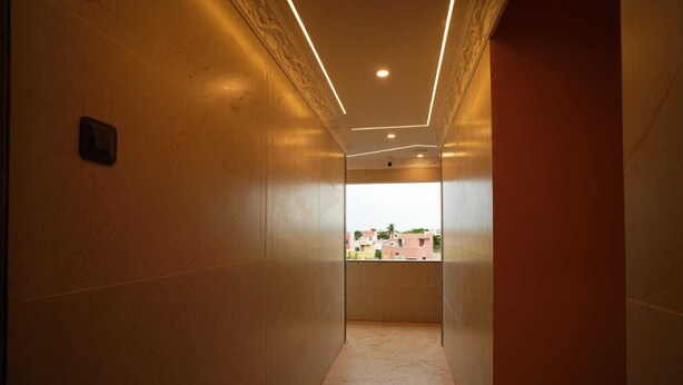 Um corredor com vista para prédios lá fora, um interruptor na parede e piso ladrilhado.