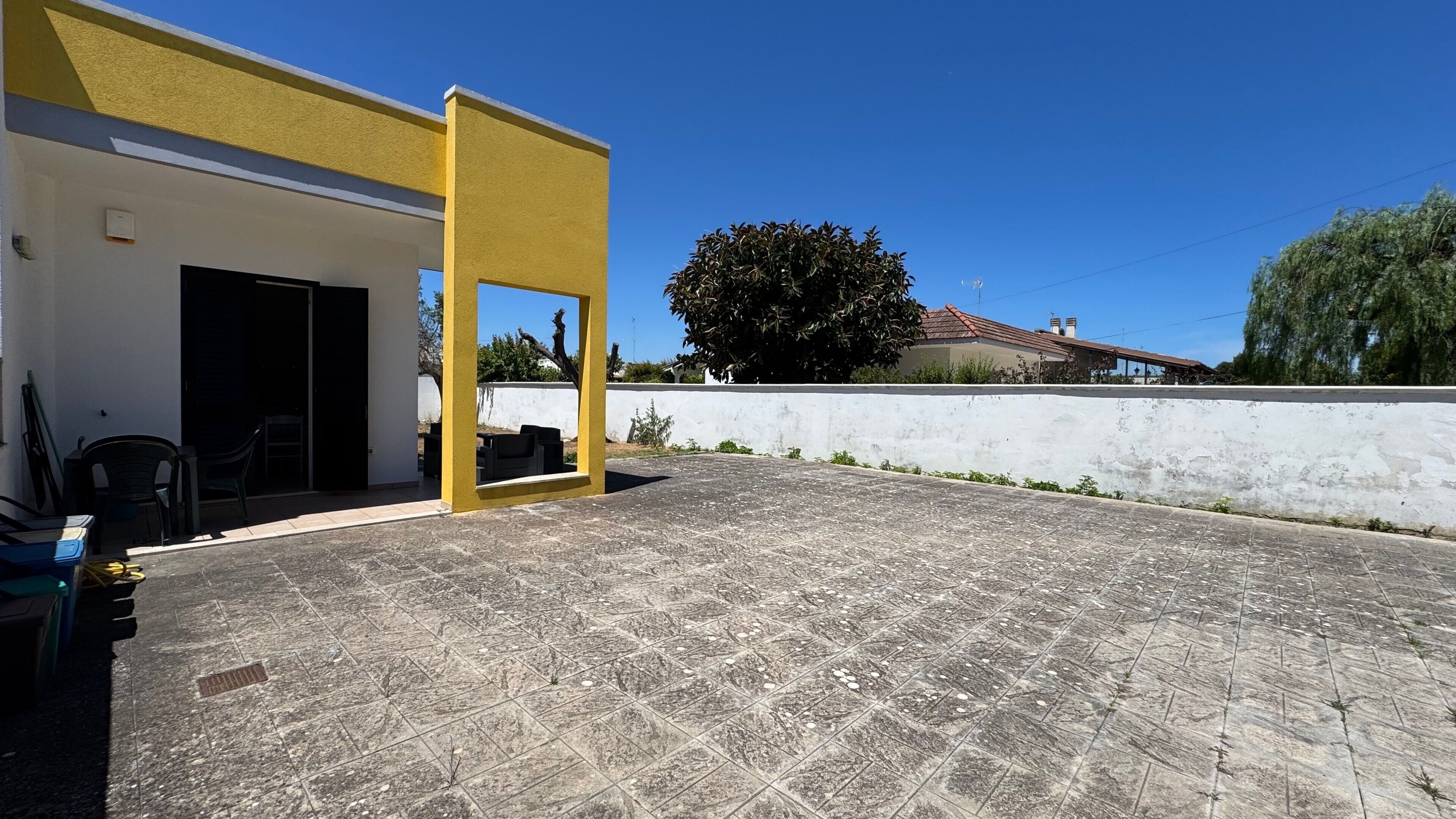 A covered outdoor area with a tiled floor, a white wall, and a yellow pillar.