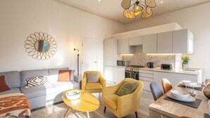 A modern living room with a sofa, armchairs, a coffee table, and a dining area with a table set for two. - Boutique Eastbourne Gem (Eastbourne)