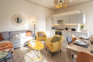 A modern living room with a sofa, armchairs, a coffee table, and a dining area with a table set for two. - Boutique Eastbourne Gem (Eastbourne)