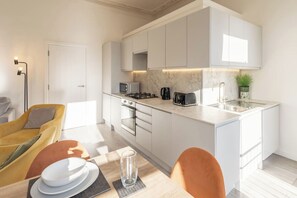 A modern kitchen with white cabinets, a built-in oven, a microwave, and a toaster. - Boutique Eastbourne Gem (Eastbourne)