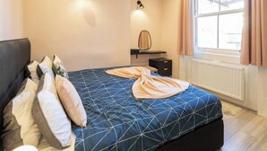 A bedroom with a bed, pillows, a bedside table, a mirror, and a window with curtains. - Boutique Eastbourne Gem (Eastbourne)