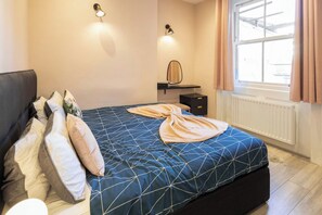 A bedroom with a bed, pillows, a bedside table, a mirror, and a window with curtains. - Boutique Eastbourne Gem (Eastbourne)