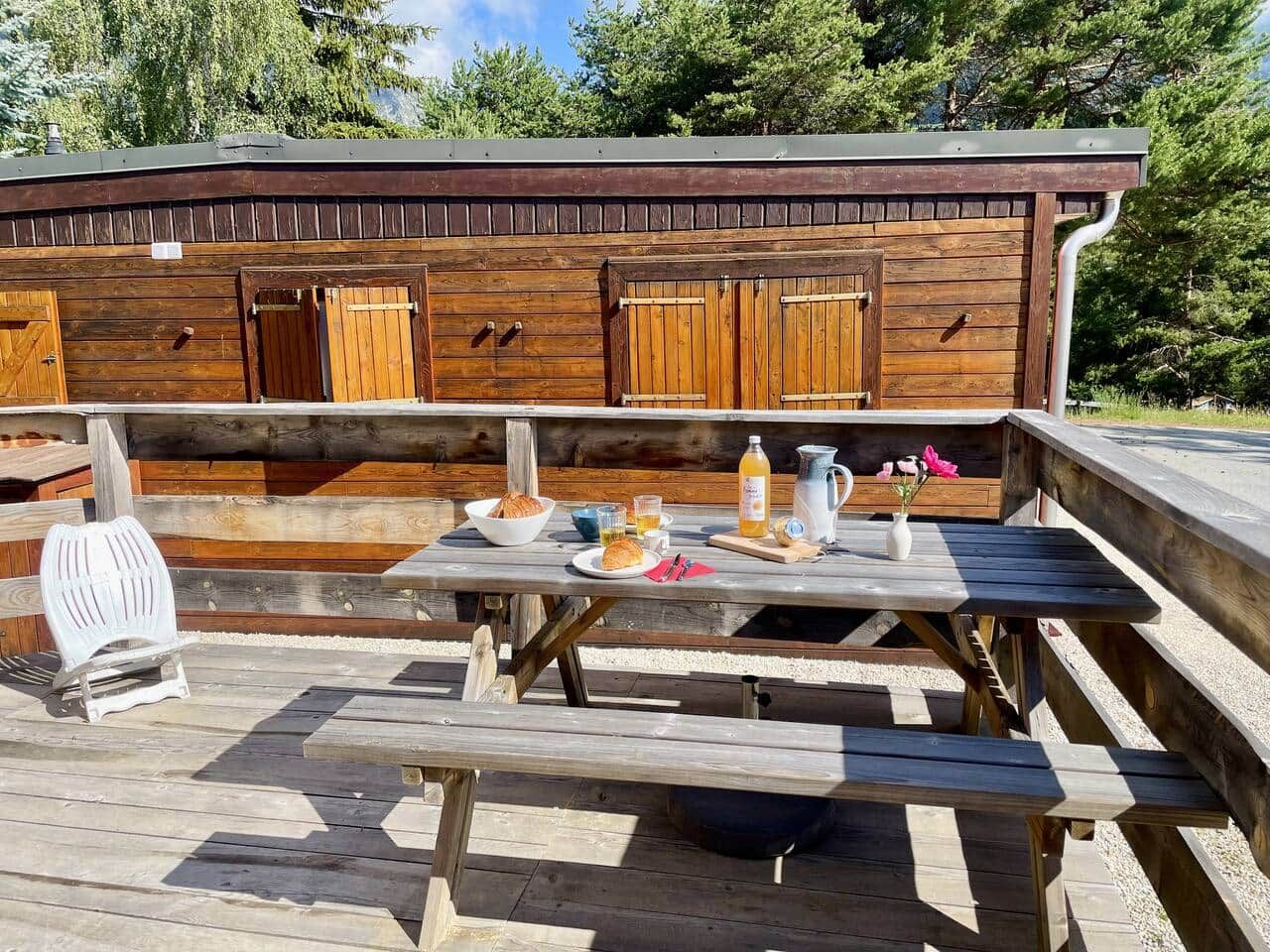A wooden building with a bench and picnic table, a grill, and outdoor seating.