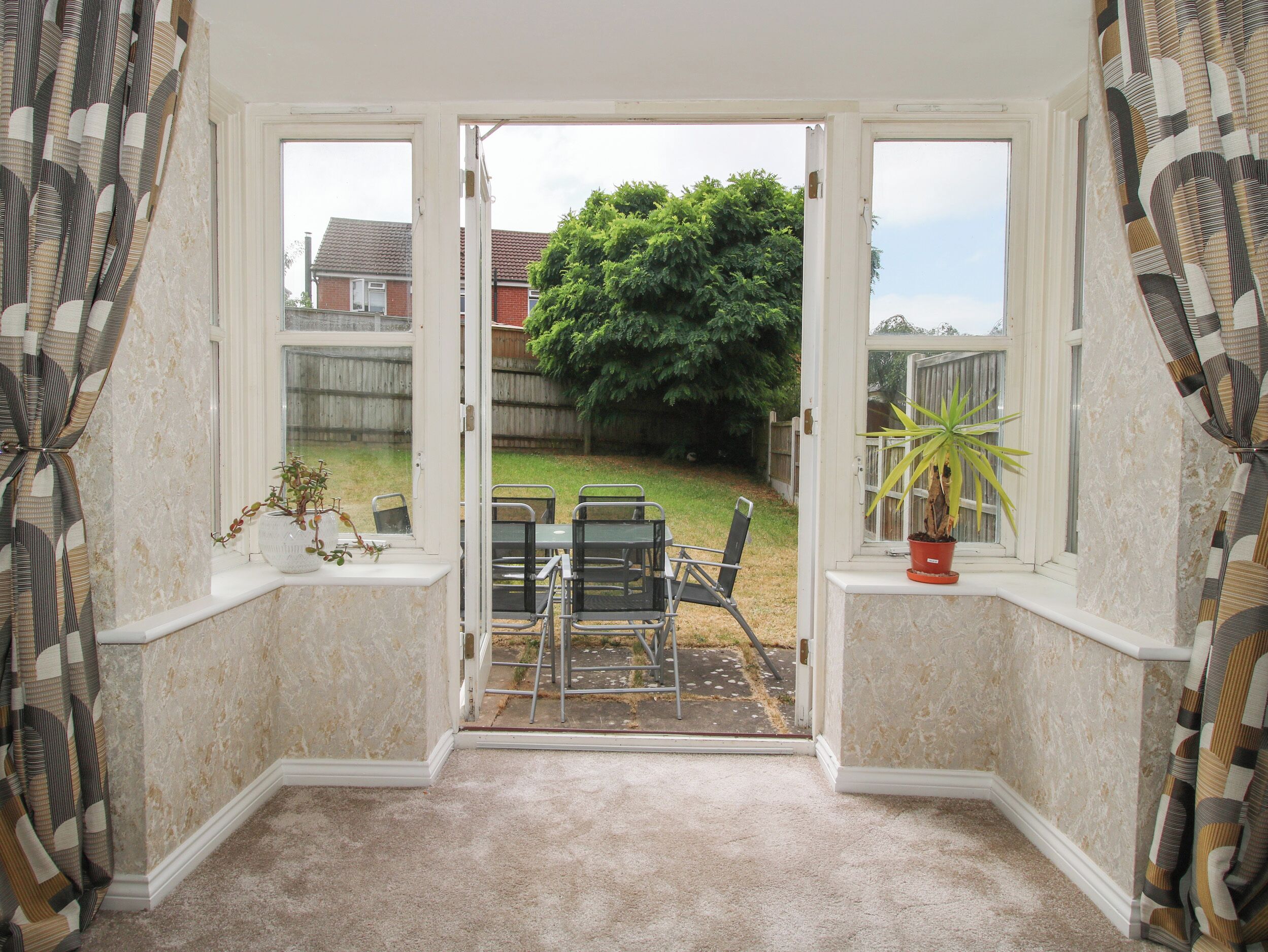 A room with a view through a door to a backyard with a lawn, a tree, and a patio with chairs.