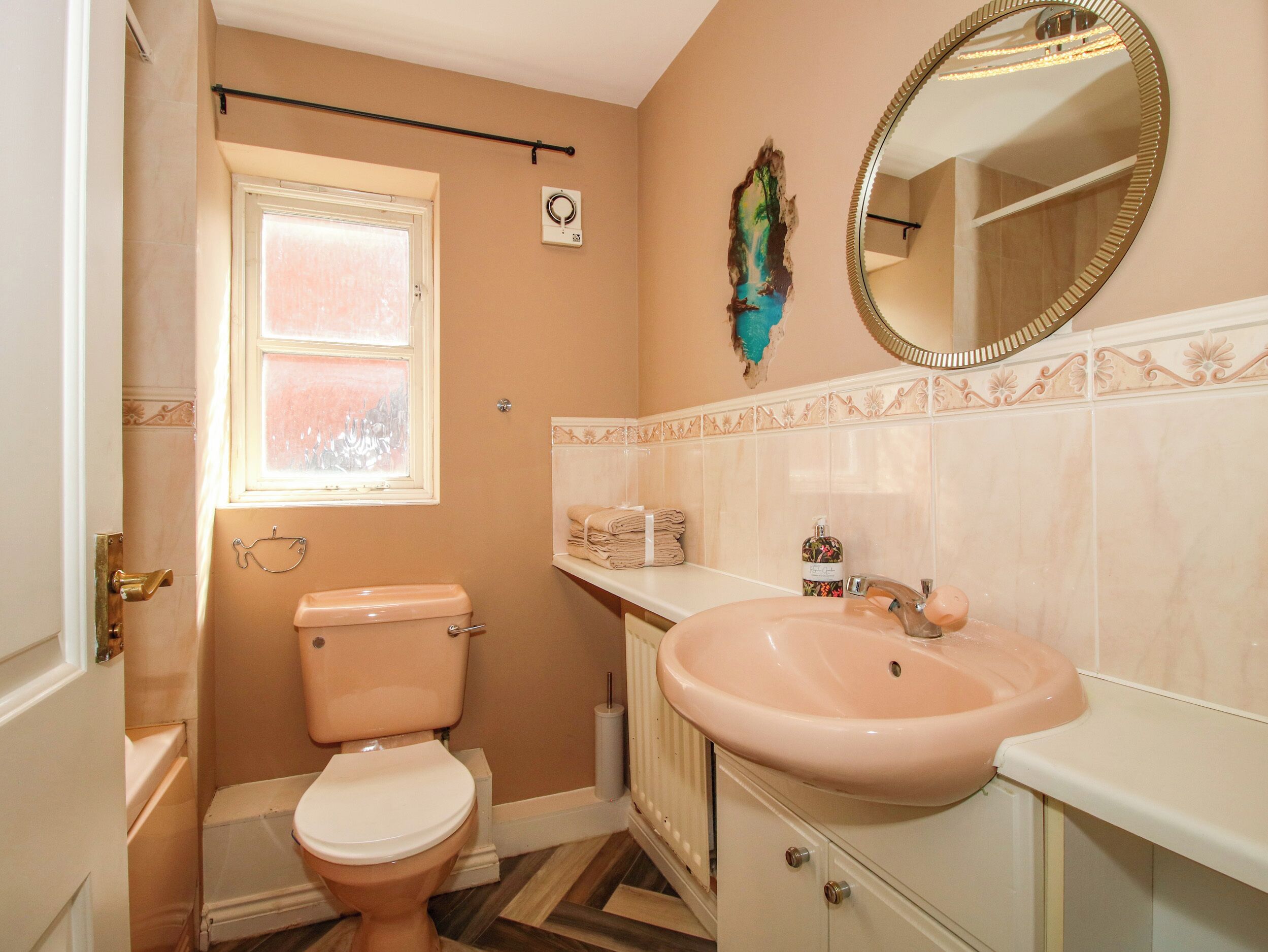 A bathroom with a toilet, sink, mirror, and a window.