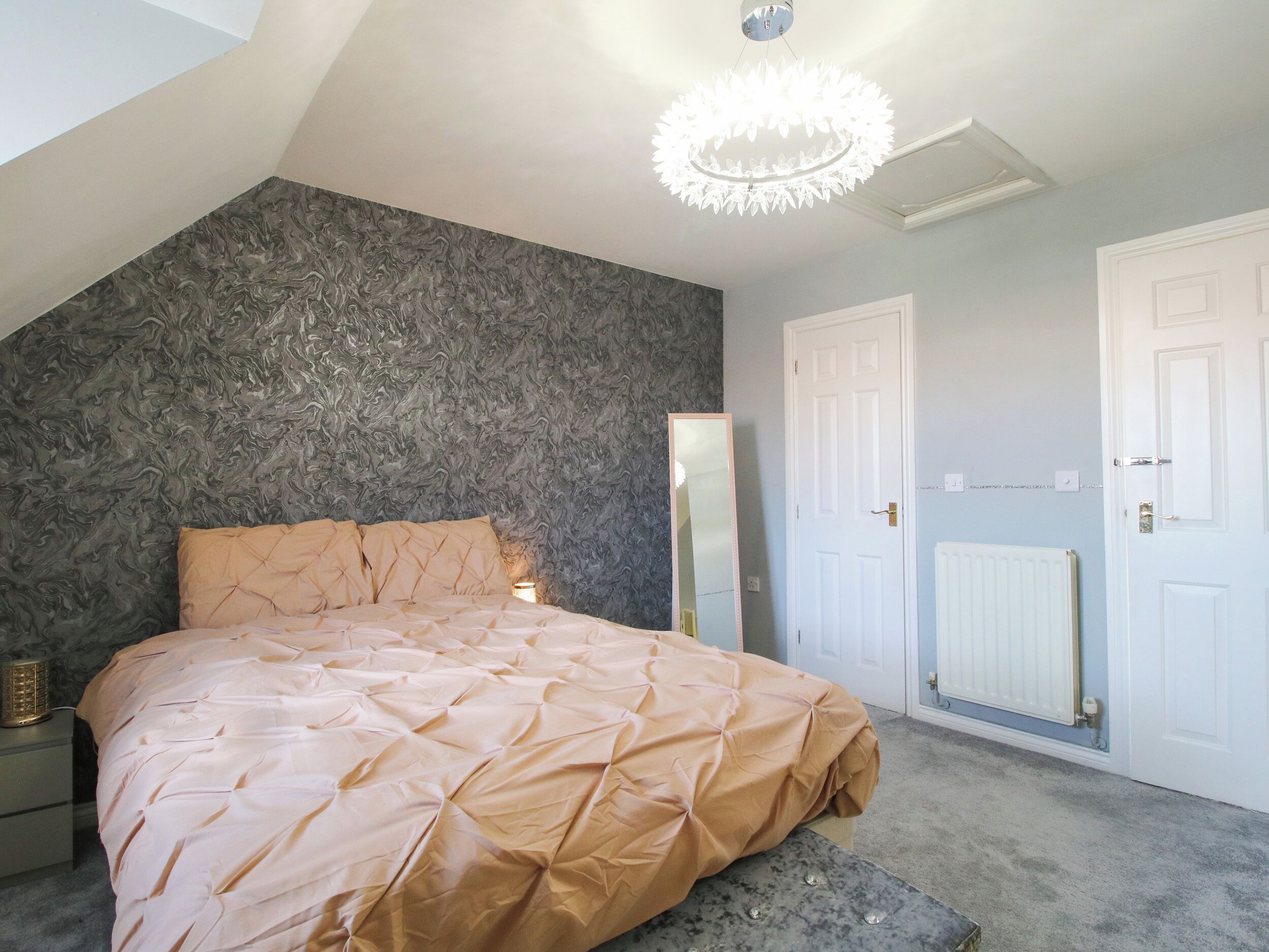 A bedroom with a bed, a mirror, a radiator, and a door.