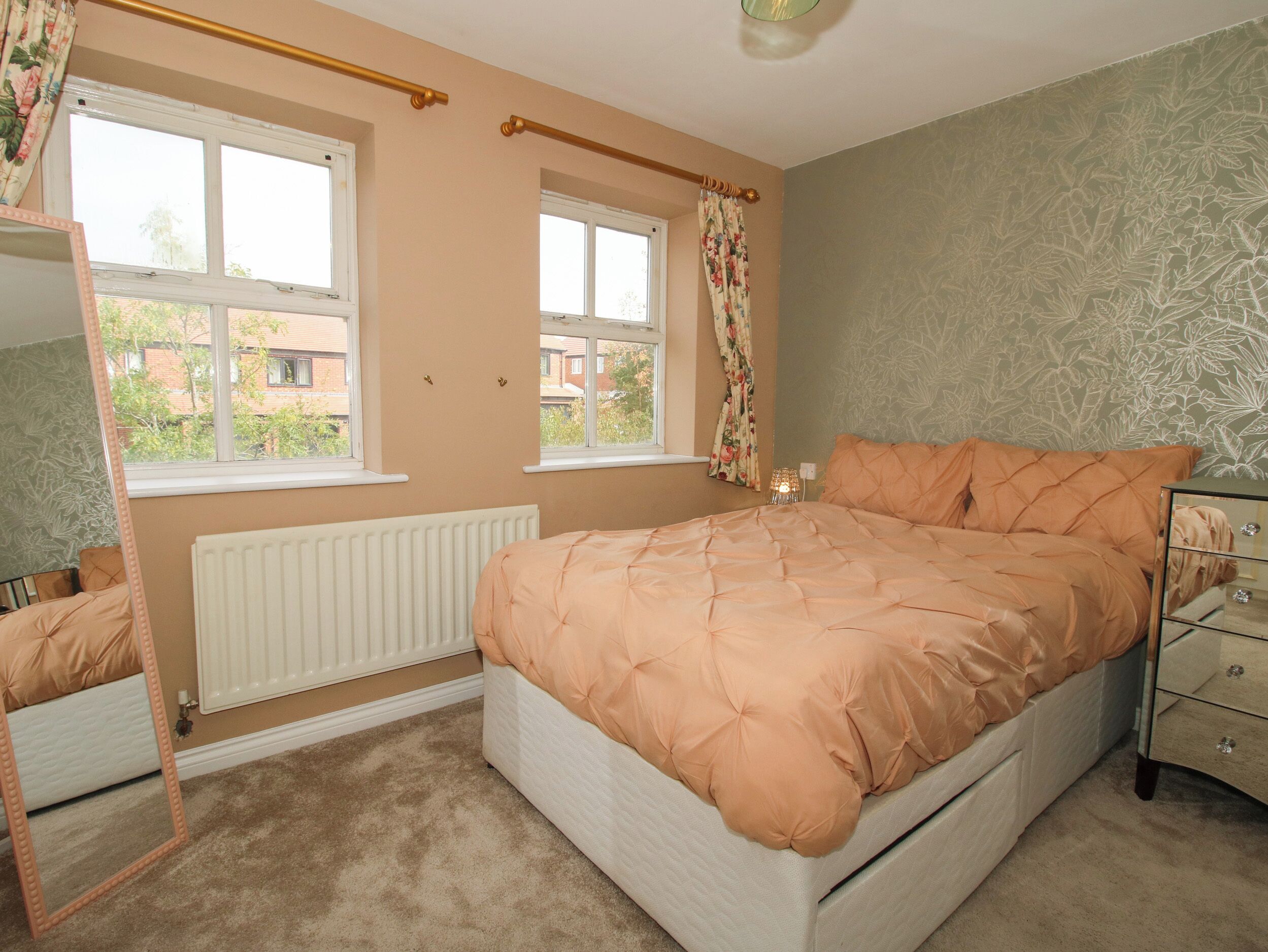 A bedroom with a bed, a dresser, a mirror, two windows, and a radiator.
