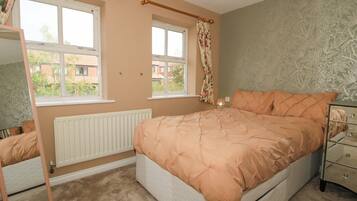 A bedroom with a bed, a dresser, a mirror, two windows, and a radiator.