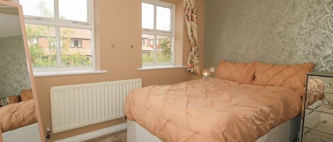 A bedroom with a bed, a dresser, a mirror, two windows, and a radiator.