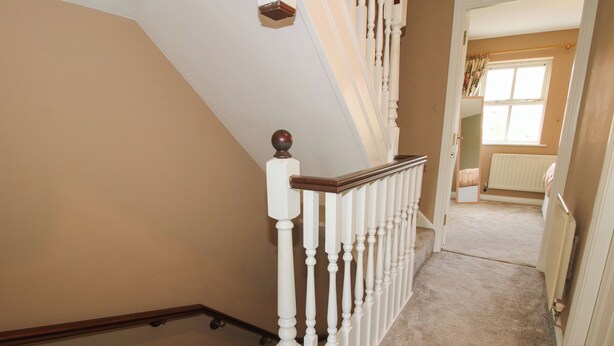 A carpeted staircase with white balusters and a wooden handrail, leading to a room with a window and a radiator.