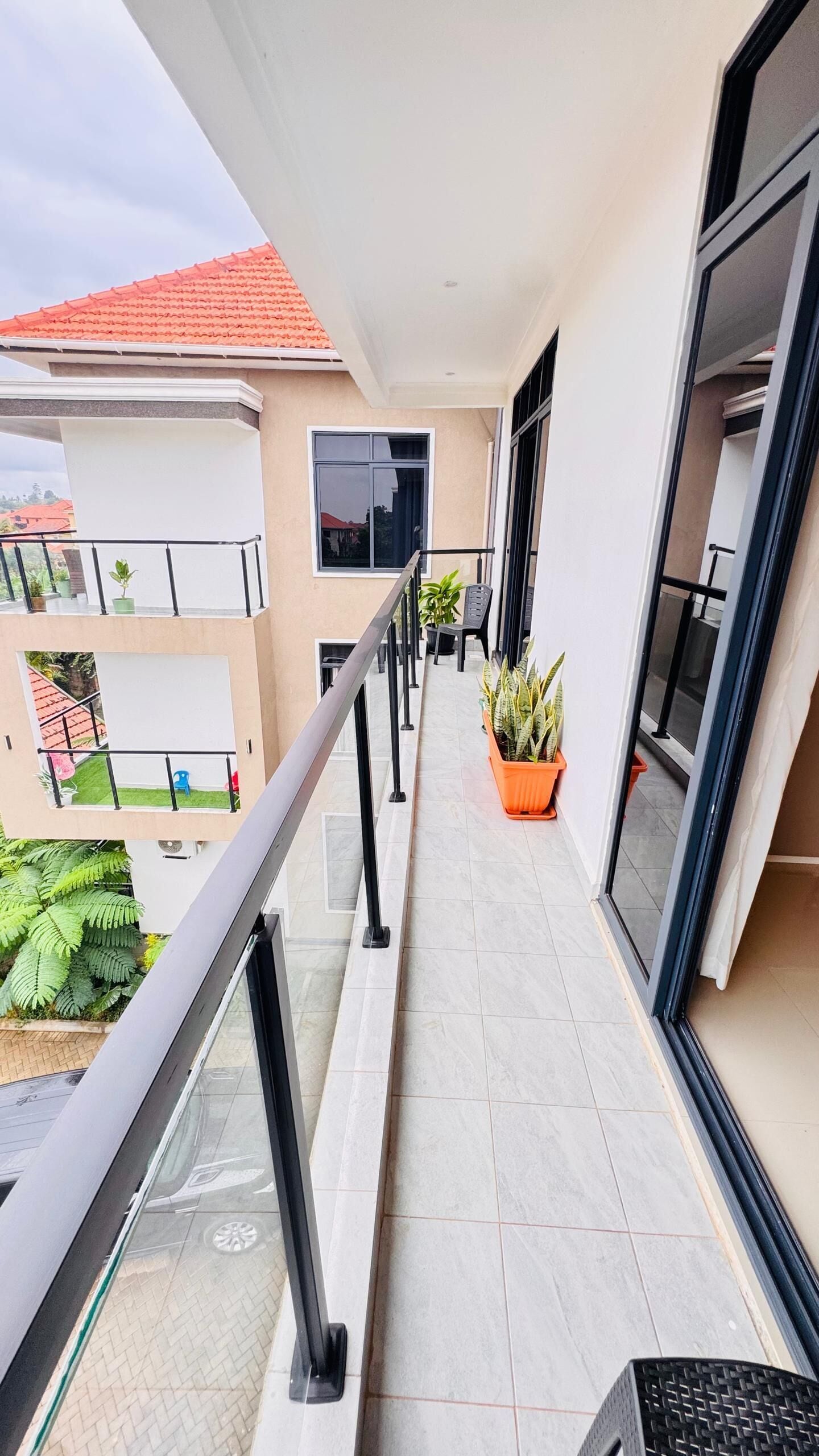 A balcony with a glass railing, potted plants, and a view of neighboring buildings.