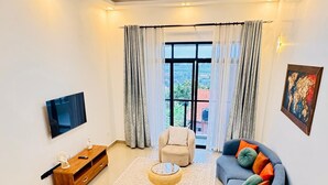 A modern living room with a flat-screen TV, a sofa, a coffee table, and a large window with curtains.