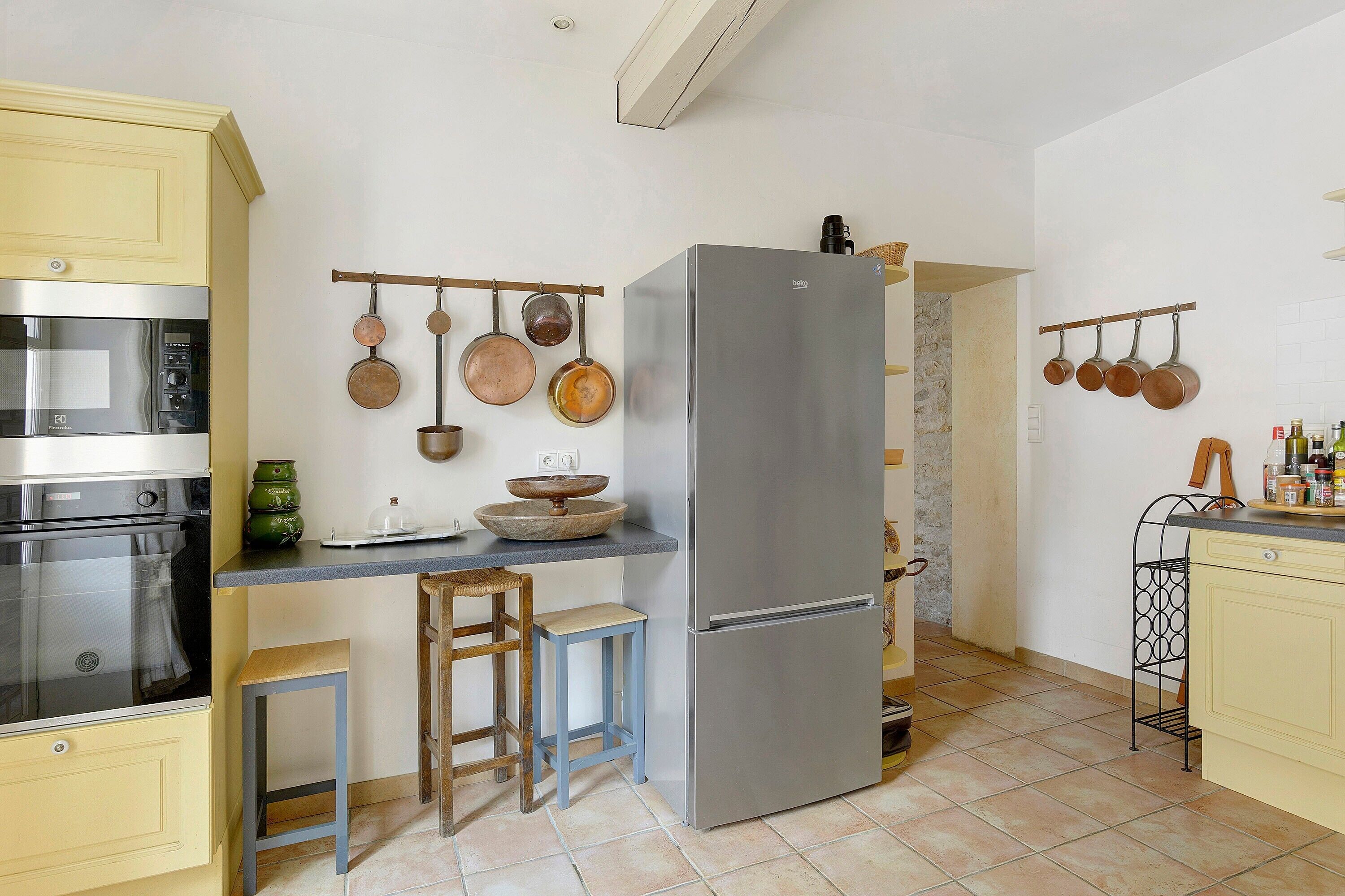 A compact kitchen with a built-in microwave, a stainless steel refrigerator, and hanging pots.